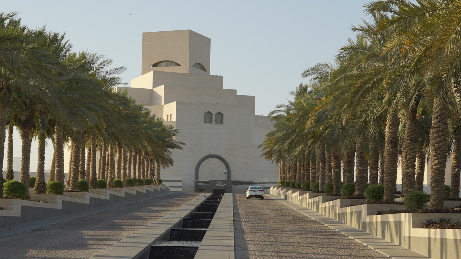 A museum is framed by palm trees and a road.