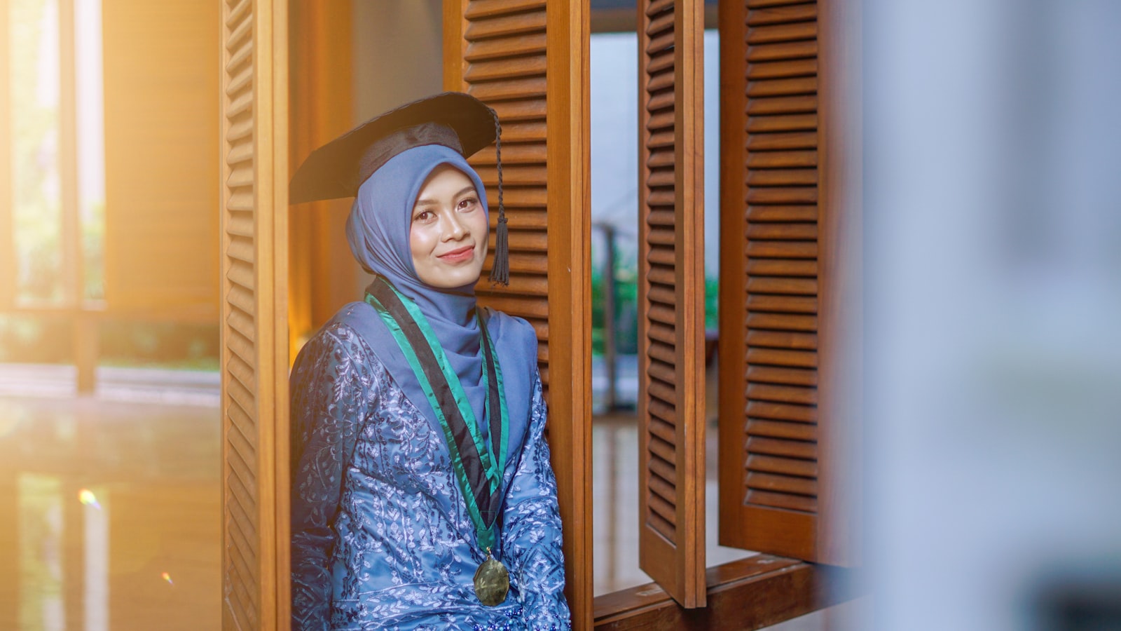 Woman in hijab and graduation regalia smiles warmly.