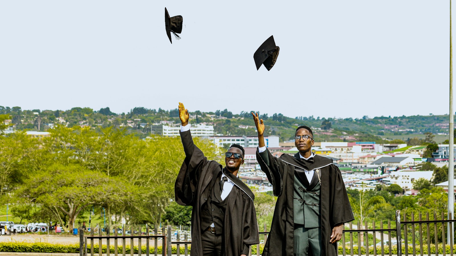Two graduates in caps and gowns toss hats in air