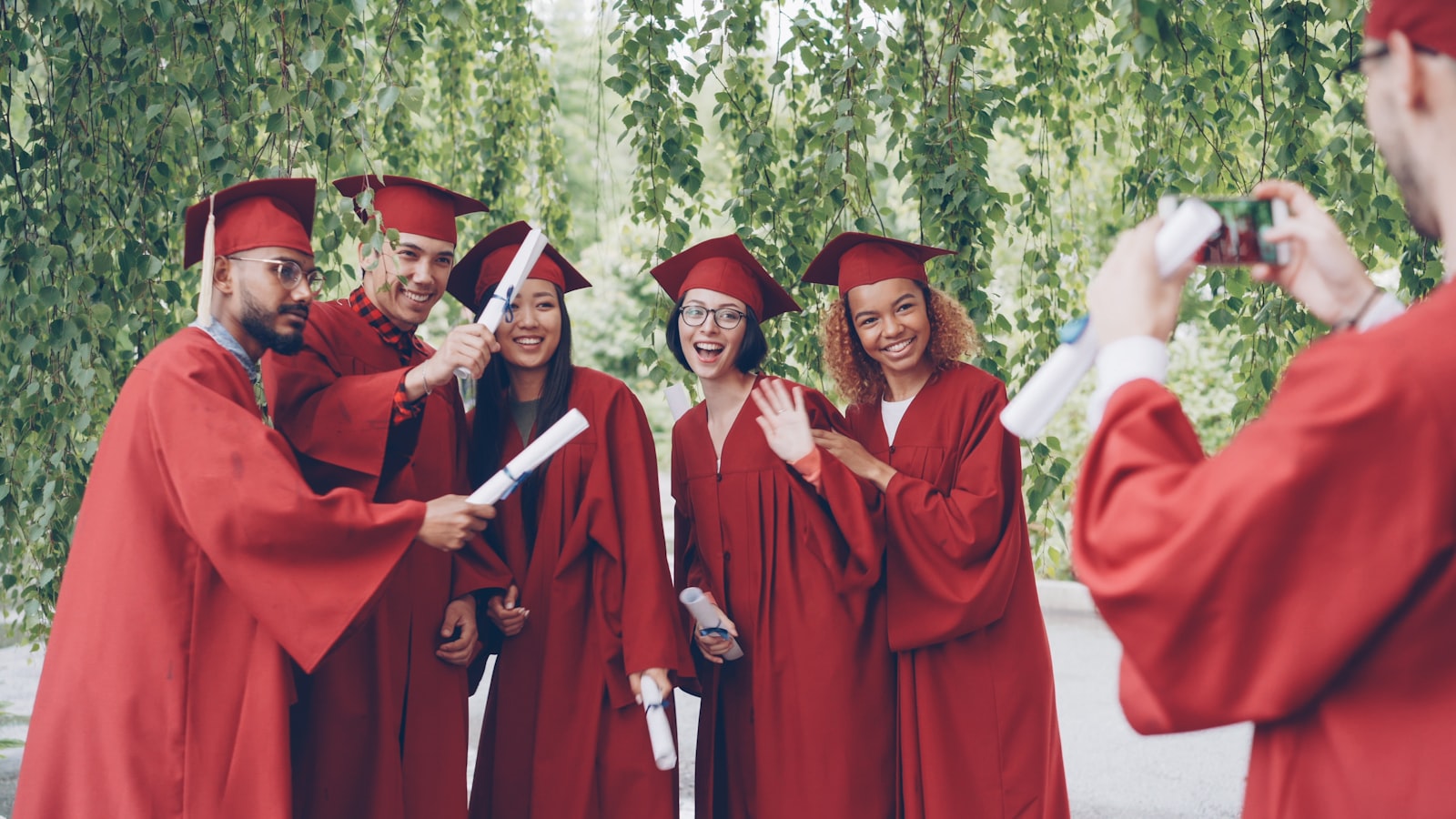 Graduates in red robes pose for a photo outdoors