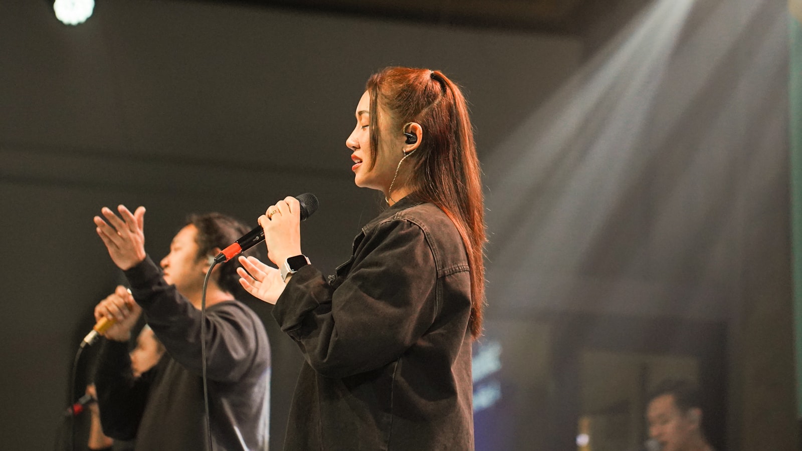 Women singing with hands raised on stage.