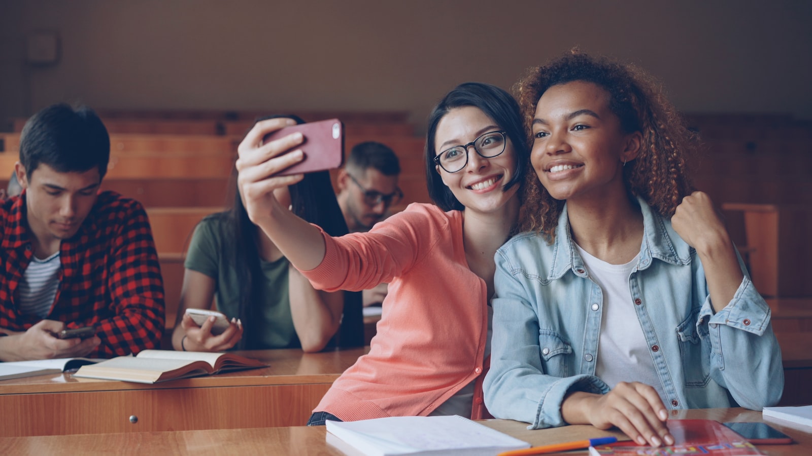 Two smiling students taking a selfie in a lecture hall.