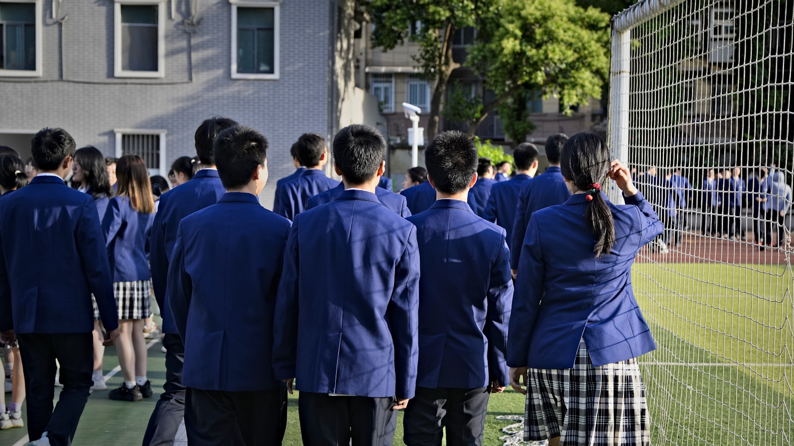 Students in uniform are walking near a sports field.