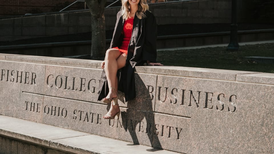 a woman in a graduation gown sitting on a stone wall
