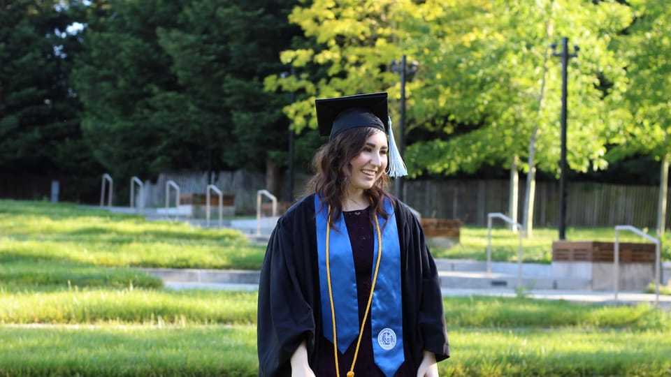 woman in blue academic gown and mortar board standing on green grass field during daytime