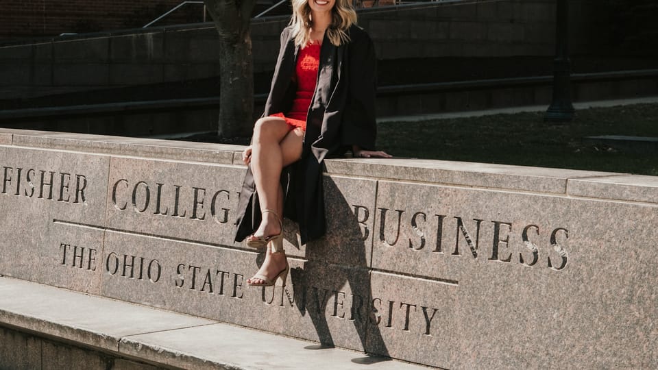 a woman in a graduation gown sitting on a stone wall