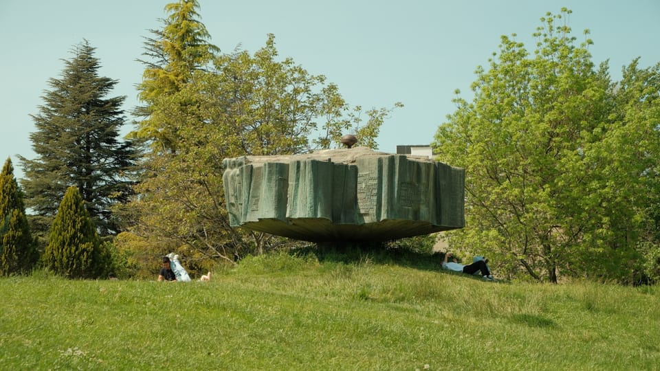 People relax on a grassy hill near a unique structure.