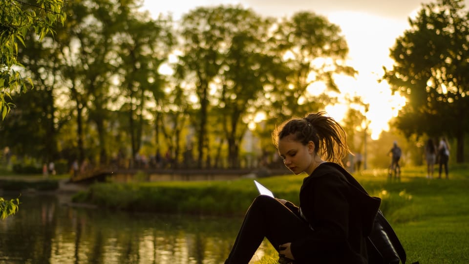 woman sitting on grass field beside body of water during golden hour