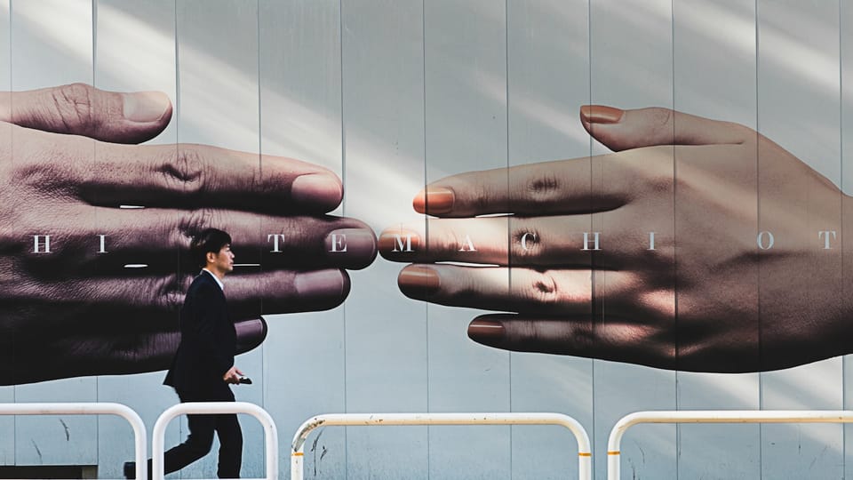 man walking on sidewalk beside hands mural