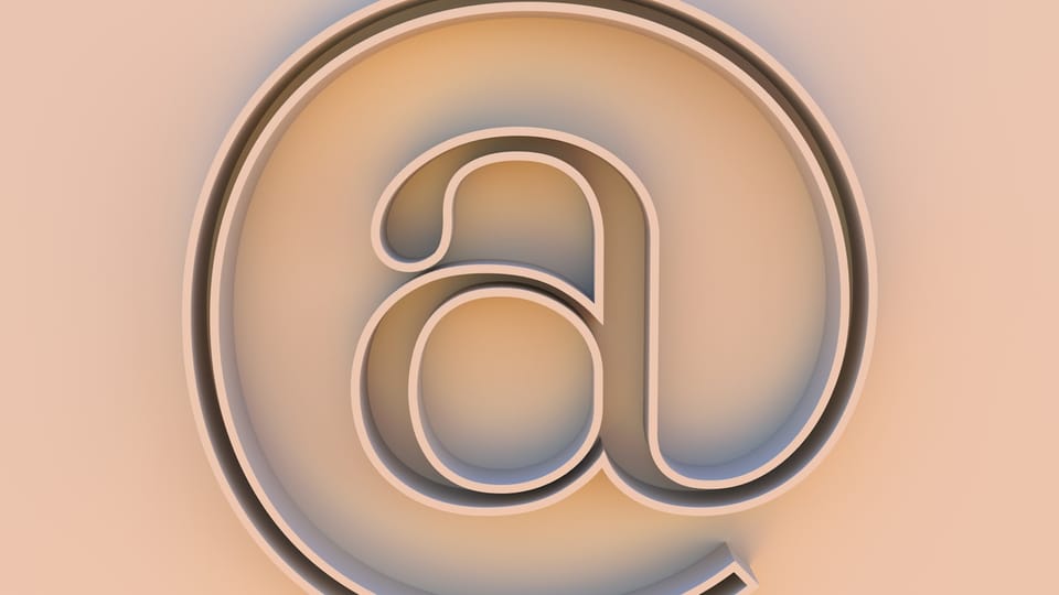 An "at" symbol on a beige background.